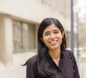 Portrait of lead researcher, PhD student Amika Shah, smiling in front of a blurred background of a building.