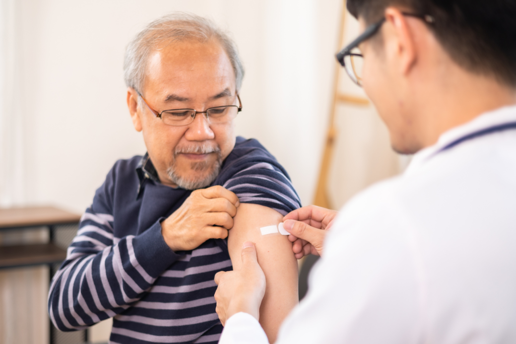 An elderly man gets a bandaid from a healthcare practitioner, presumably after getting an influenza vaccine